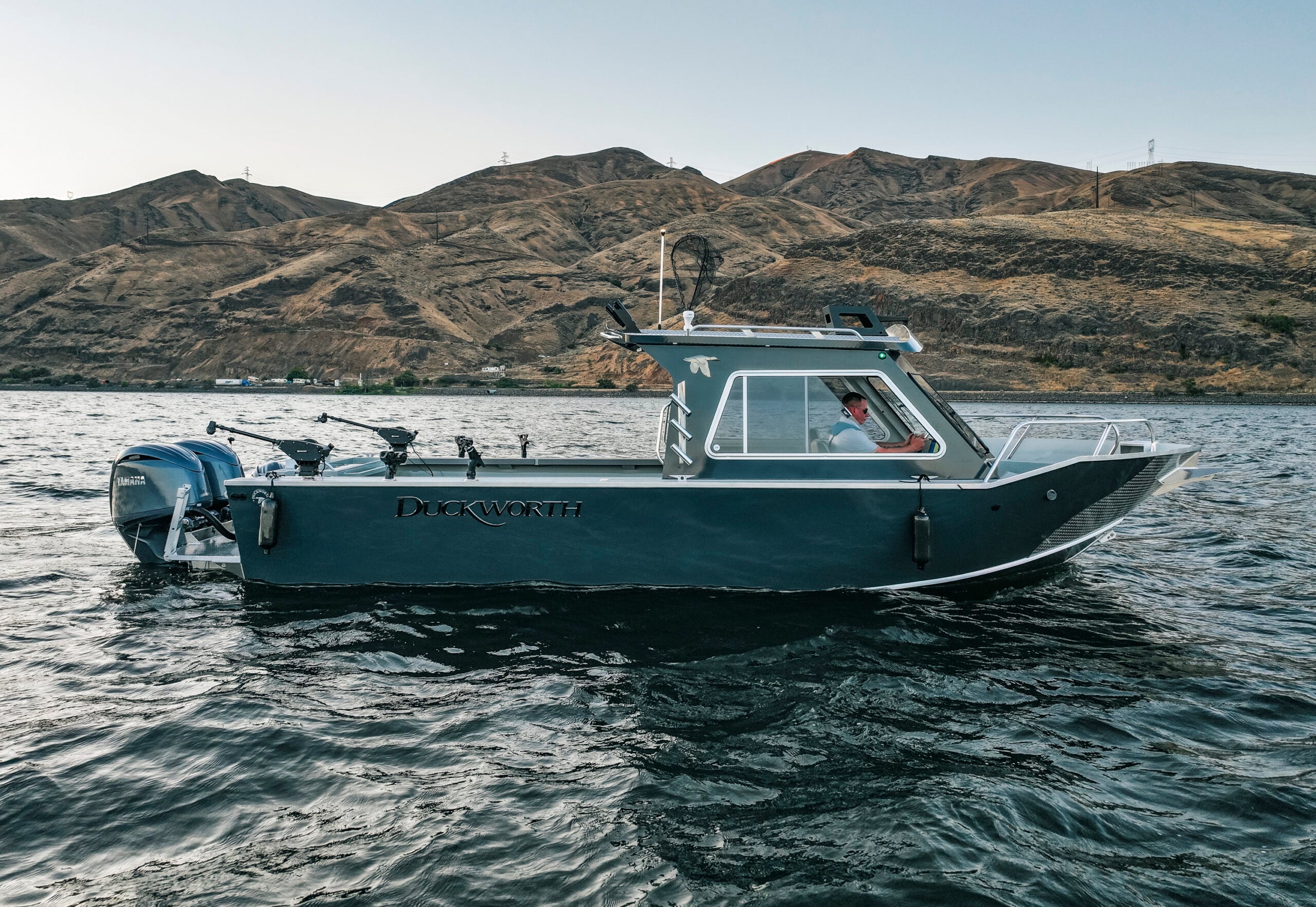 The Duckworth 20 advantage access boat model glides across the water with a brown mountain range in the background.